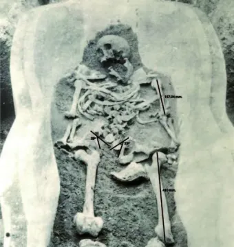 Human-shaped sarcophagus with a partially excavated skeleton inside, shown with measurement lines and angles.