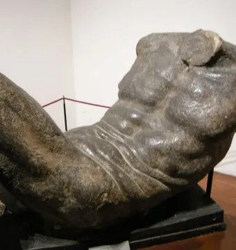 River God sculpture showing a reclining male torso and upper legs with a rough, textured surface.