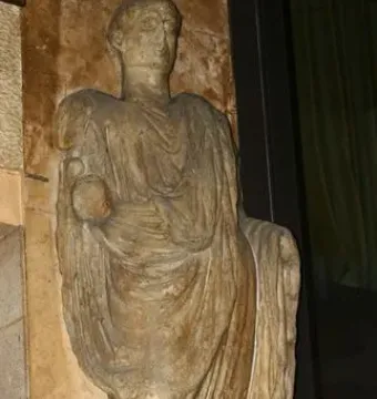 Scior Carera, a weathered stone statue of a draped standing man holding a spherical object, on an inscribed plinth.