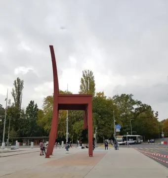 Broken Chair sculpture with a tall backrest and one broken leg on a paved plaza, with pedestrians and a bus in the background.