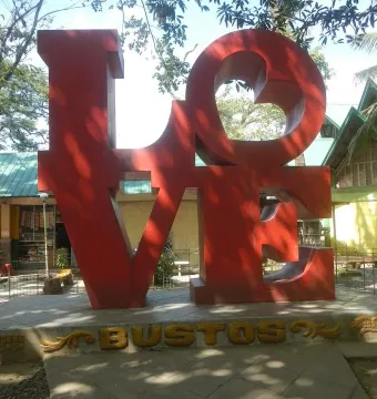 Bright red LOVE sculpture with a tilted O on a concrete base in Bustos, Bulacan.