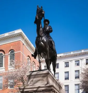 Joseph Hooker equestrian statue on a tall stone pedestal with HOOKER inscribed on the base, set against buildings and blooming trees.
