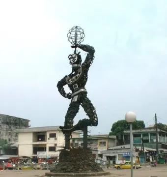 La Nouvelle Liberté sculpture rising on a stone base in an urban square, with one arm raised holding a spherical metal form.