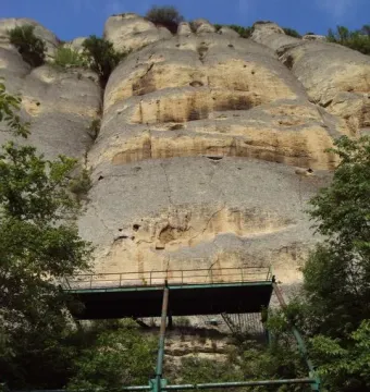 Rock face partly hidden by trees with a metal observation platform on the Madara Rider cliff.