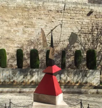 Nancy, a large abstract metal sculpture with red, black, and silver geometric forms on a stone pedestal in an outdoor courtyard.
