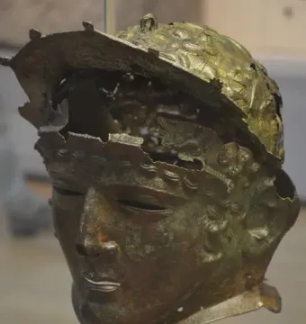 Corroded bronze Ribchester Helmet with a full face mask and damaged upper headpiece.