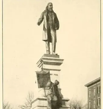 Albert Pike Memorial with a large statue of a bearded man atop a multi-tiered stone pedestal, with a smaller seated bronze figure below.