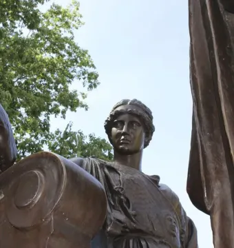 Detail of Alma Mater showing the woman’s face, braided hair, patterned bodice, and a bronze scroll with an arm resting on it.