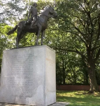 Bernardo de Gálvez equestrian statue on a tall stone pedestal surrounded by trees.