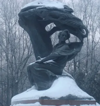 Chopin Monument in a snowy park, with a seated bronze figure beneath a large wave-like sculpture.