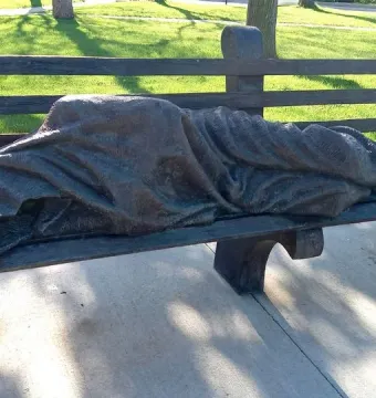 Homeless Jesus bronze sculpture of a sleeping figure on a park bench, with wounded feet exposed at one end.