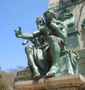 Bronze statue of Júlio de Castilhos seated on a stone pedestal, with one hand raised and pointing forward.