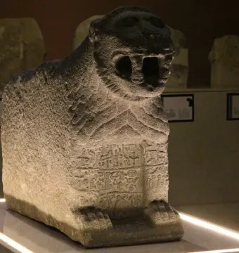 Stone lion sculpture with open mouth and carved symbols on its front