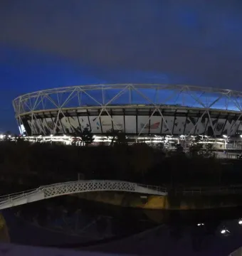 Orbit Tower glowing red beside a brightly lit stadium at dusk.