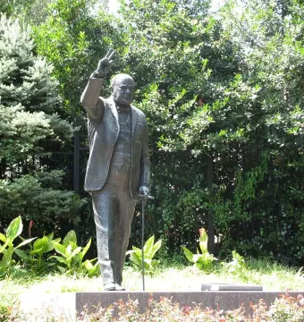 Bronze Winston Churchill statue raising his right hand in a V for victory gesture and holding a cane.