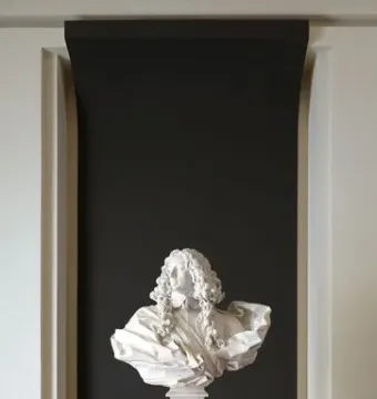 White marble bust of Francesco I d\'Este with long curly hair and draped shoulders, displayed on a pedestal against a dark wall.