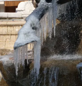 Close-up of a frozen detail on the Fontaine Bartholdi, with water flowing over stone and icicles hanging from the sculpture.
