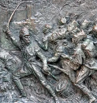 Bronze bas-relief of soldiers in battle on the José de San Martín monument, with swords, flags, and a drum in the foreground.