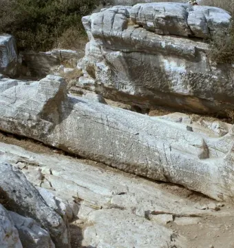 Unfinished Kouros of Apollonas stone statue lying horizontally in a rocky quarry landscape.