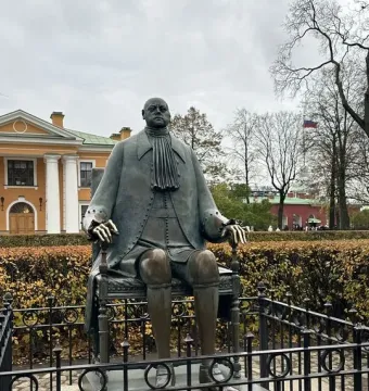 Peter I Monument shown as a bronze statue of a seated man on a stone pedestal with a low fence around it.