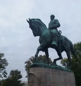 Robert E. Lee Monument showing a rider on horseback atop a tall stone pedestal with trees and cloudy sky behind it.