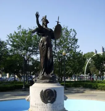Russell Alger Memorial Fountain with a bronze female statue holding a shield and sword in a blue basin.