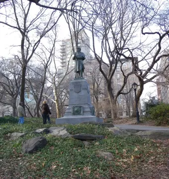 Seventh Regiment Memorial bronze figure on a stone pedestal in a winter park with city buildings behind it.