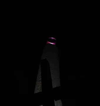 The Thanksgiving Candle monument illuminated at night, with a glowing magenta-purple ring at the top.