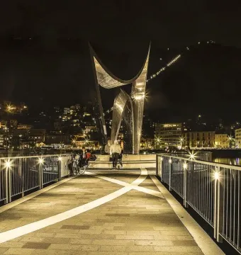 Life Electric sculpture lit at night on a waterfront promenade with Como city lights and a dark mountainside in the background.
