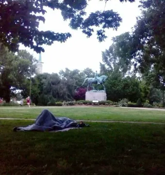 Robert E. Lee Monument in a park, with a person lying wrapped in a blanket on the grass in the foreground.
