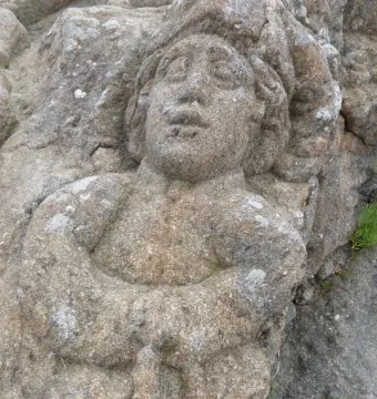 Carved figure in the Rothéneuf Sculpted Rocks, with a prominent face and arms crossed over the chest in a rough rock surface.