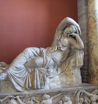 Sleeping Ariadne marble sculpture reclining against a reddish wall with ornate columns nearby.