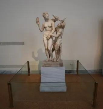 Marble sculpture group of Aphrodite with Pan and Eros, showing a nude female figure resisting a horned, goat-legged Pan while a small winged Eros pushes him away.