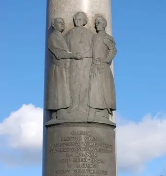 Electio Viritim Monument with a bronze relief of three figures on a tall light-grey column.