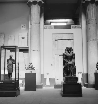 Khafre Enthroned statue displayed on a pedestal in a museum, with a falcon deity behind the pharaoh\'s head.