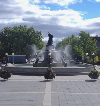 La Fermière fountain in a paved square with dark statues and water jets spraying outward.