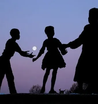 Silhouetted figures stand against a purple-blue sky with the moon between them.