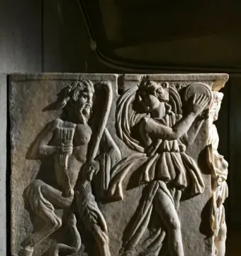 Roman marble relief from the Sarcophagus of the Triumph of Bacchus showing a bearded satyr-like figure playing panpipes beside a dancing woman with a tambourine and a serpent emerging from a vessel.