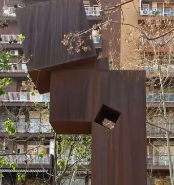 El Llarg Viatge, a tall rust-colored abstract metal sculpture with a square cutout on a brick platform.
