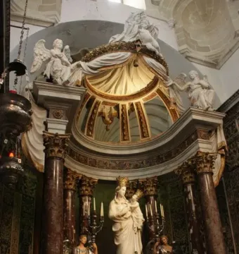 Crowned white marble Madonna di Trapani statue with the infant Jesus on an ornate altar with flowers and candles.