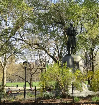 Seventh Regiment Memorial statue on a tall stone pedestal in Central Park, seen from behind among trees and shrubs.