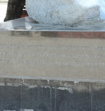 Stone base of The Shot in the Back monument with a Cyrillic inscription and a partially visible stone sculpture above it.