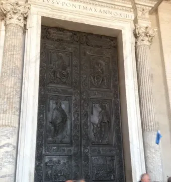 The Filarete Door with dark bronze relief panels framed by marble columns, with people passing in front.