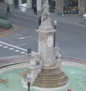 The Fountain of Hercules in a circular pool, with a stone figure on a tiered pedestal flanked by lion sculptures.