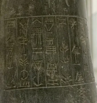 Close-up of the inscribed stone surface of the Idi-Ilum statuette, showing vertical columns of ancient cuneiform characters.