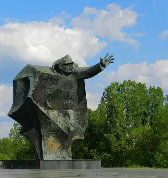 Kościuszkowców Memorial bronze figure with one arm outstretched against a blue sky and trees.