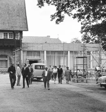 Crowds gather beside buildings on the plateau below the Kyffhäuser Monument, including a stone building and a modern café terrace.