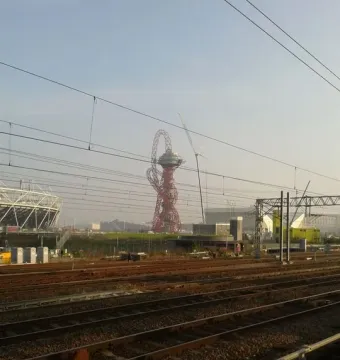 Orbit Tower rising behind railway tracks and overhead wires, with part of a stadium visible to the left.