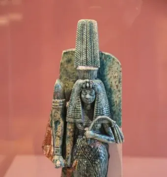 Ancient Egyptian statue of Queen Tiye with a tall headdress and patterned garment, holding a fan-like object.