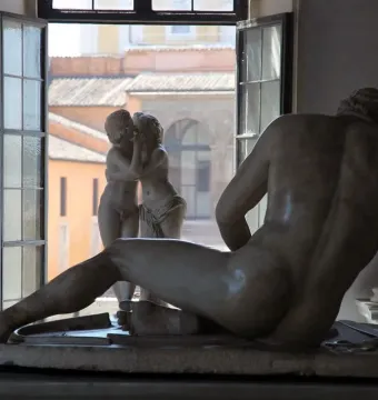 Cupid and Psyche marble sculpture seen in a window with rooftops beyond, partially obscured by a reclining marble figure in the foreground.